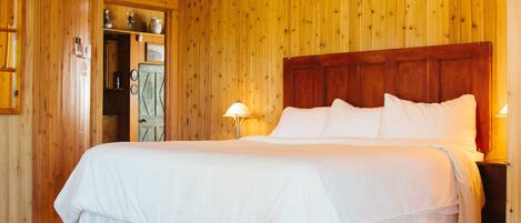 Ein Zimmer mit Holzwänden, einem großen Bett, einer Holztür und einem kleinen Tisch mit einer Lampe.
