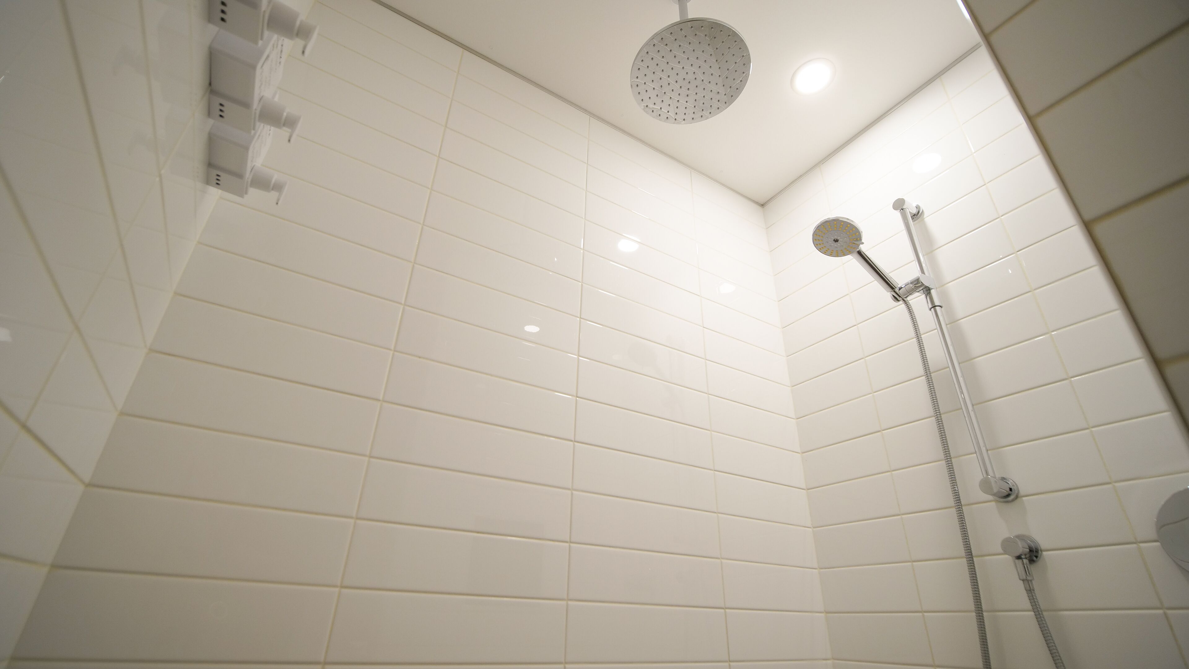 Een moderne badkamer met witte betegelde wanden en een douchekop aan het plafond.