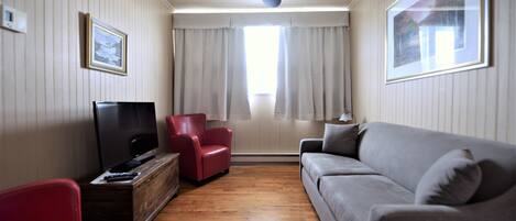 Una sala de estar con una televisión de pantalla plana, sofás rojos y grises, una mesa de centro de madera y un ventilador de techo.