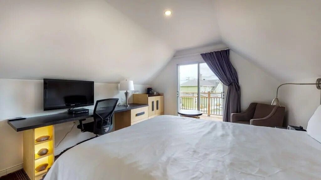 A hotel room with a large bed, a desk with a flat-screen TV, a chair, and a balcony with a view.