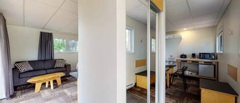 A compact living space with a sofa, bench, and kitchenette.