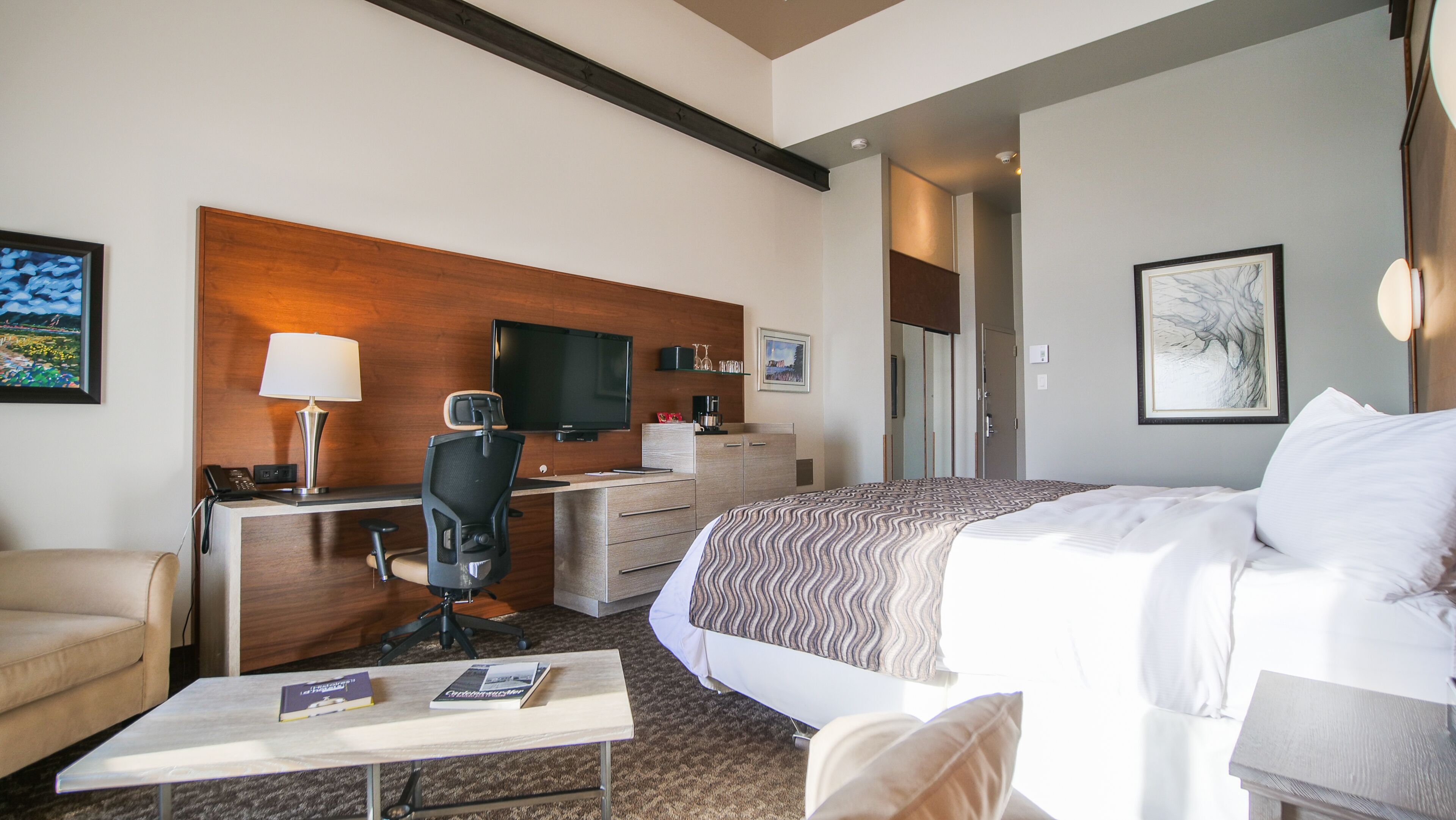 A hotel room with a bed, desk, chair, and a television.
