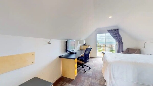 A hotel room with a bed, desk, chair, TV, and a balcony with curtains. - Manoir Belle Plage (Carleton-sur-Mer)