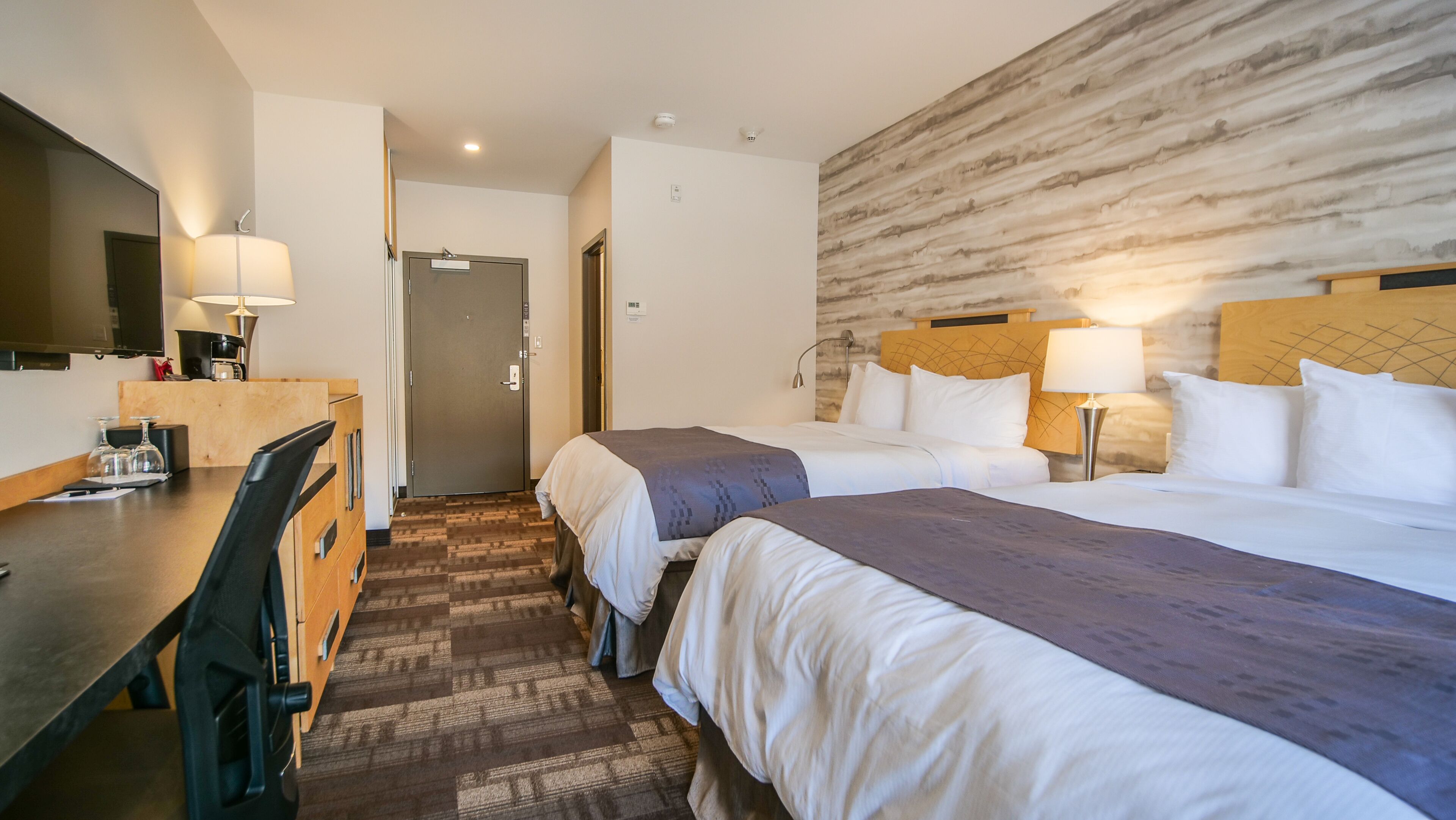 A hotel room with two beds, a desk, a chair, and a television.