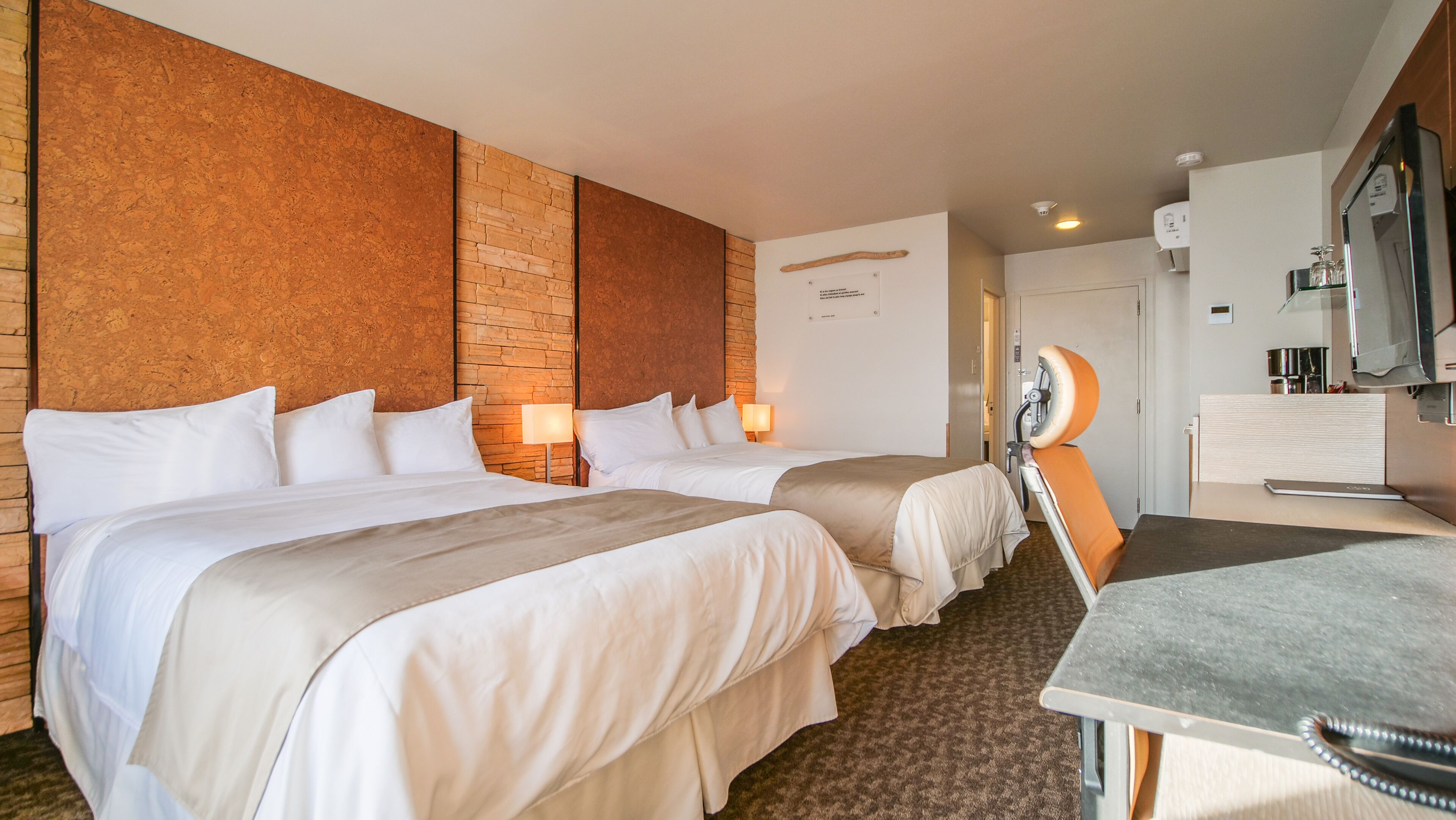 A hotel room with two beds, a desk, a television, and a minibar.