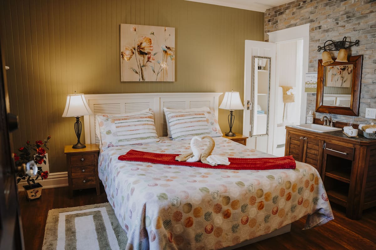 Quarto bem arrumado com uma cama grande, duas mesas de cabeceira com luminárias, um aparador de madeira e um espelho sobre o aparador.