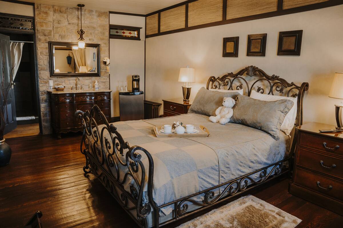 Quarto com cama, mesas de cabeceira, cômoda, espelho e banheiro com pia e espelho.