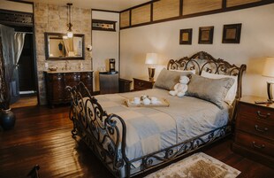 Un dormitorio con cama, mesitas de noche, cómoda, espejo y baño con lavamanos y espejo.