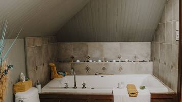 A bathroom with a toilet, sink, and bathtub, wooden flooring, and a sloped ceiling.