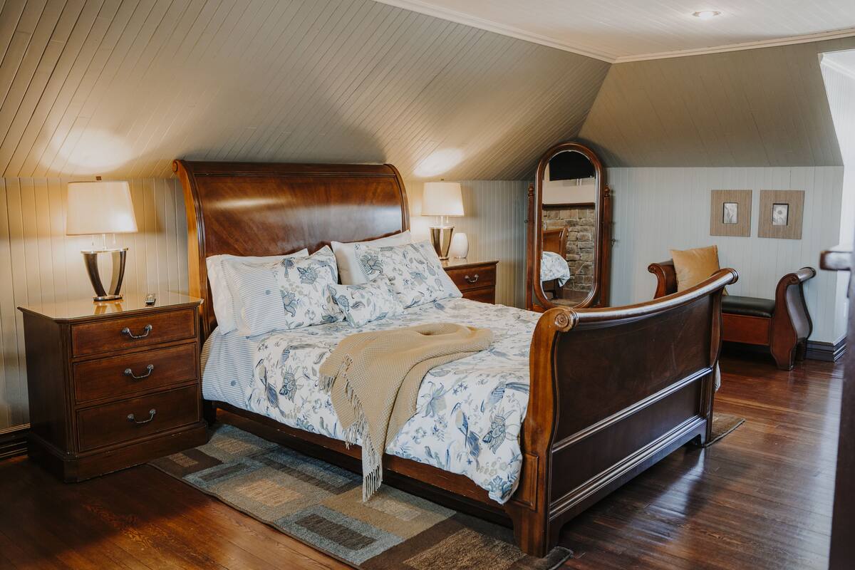Quarto com cama de madeira, duas mesas de cabeceira com luminárias, um espelho e uma cômoda.