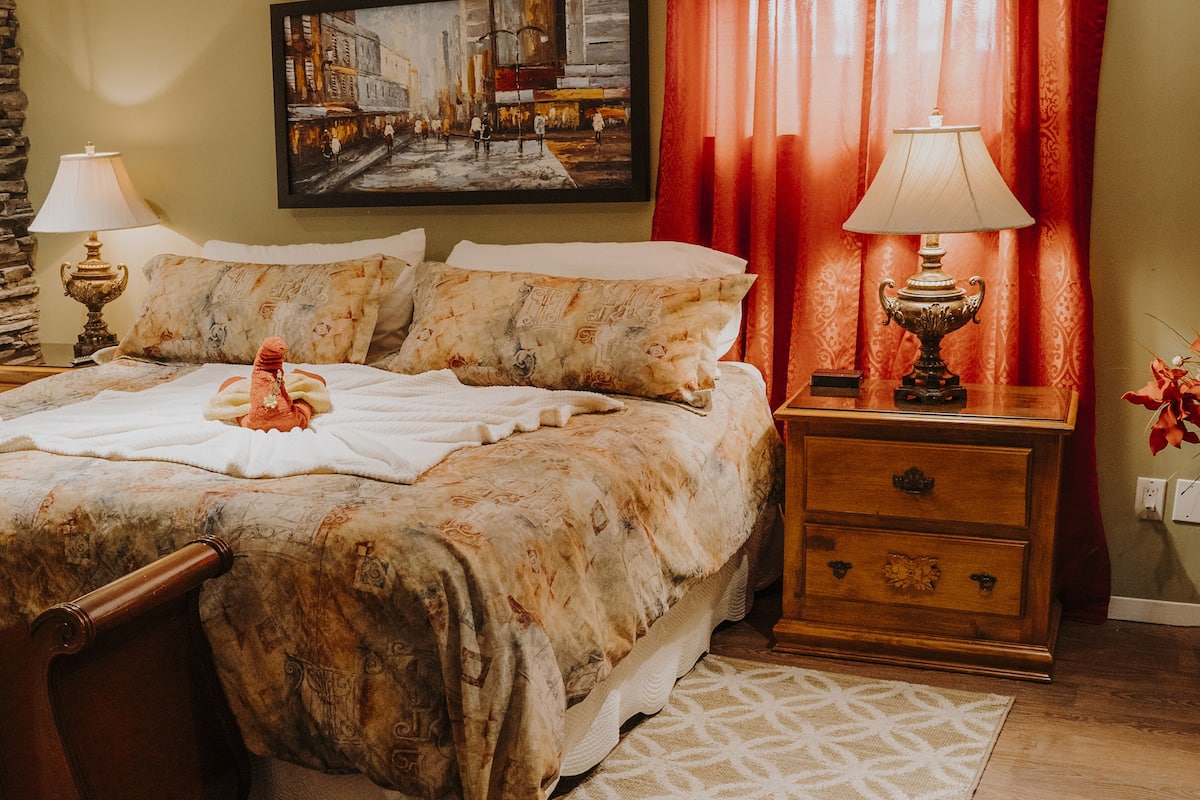 Um quarto com uma cama grande, duas mesas de cabeceira com abajures, um quadro na parede e uma cortina vermelha.