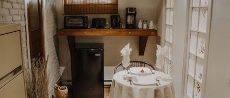 Una cocina funcional con refrigerador, cafetera y tostadora. Hay una mesa de comedor con sillas y una ventana con persianas.