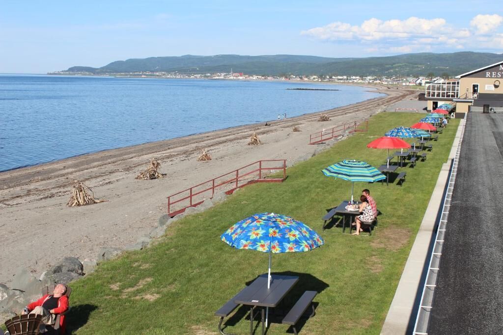 En restaurant ved stranden med udendørs siddepladser og udsigt til havet, samt en bygning med skiltet "MRS RESTAURANT".