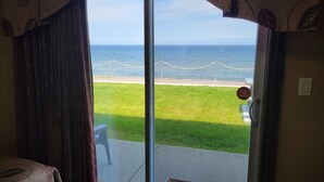 A room with a sliding glass door leading to a balcony with a view of the sea and a grassy area. - Manoir sur Mer (Sainte-Anne-des-Monts)