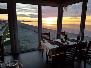 A dining area with a table set for two, overlooking a beach and sunset. - Manoir sur Mer (Sainte-Anne-des-Monts)