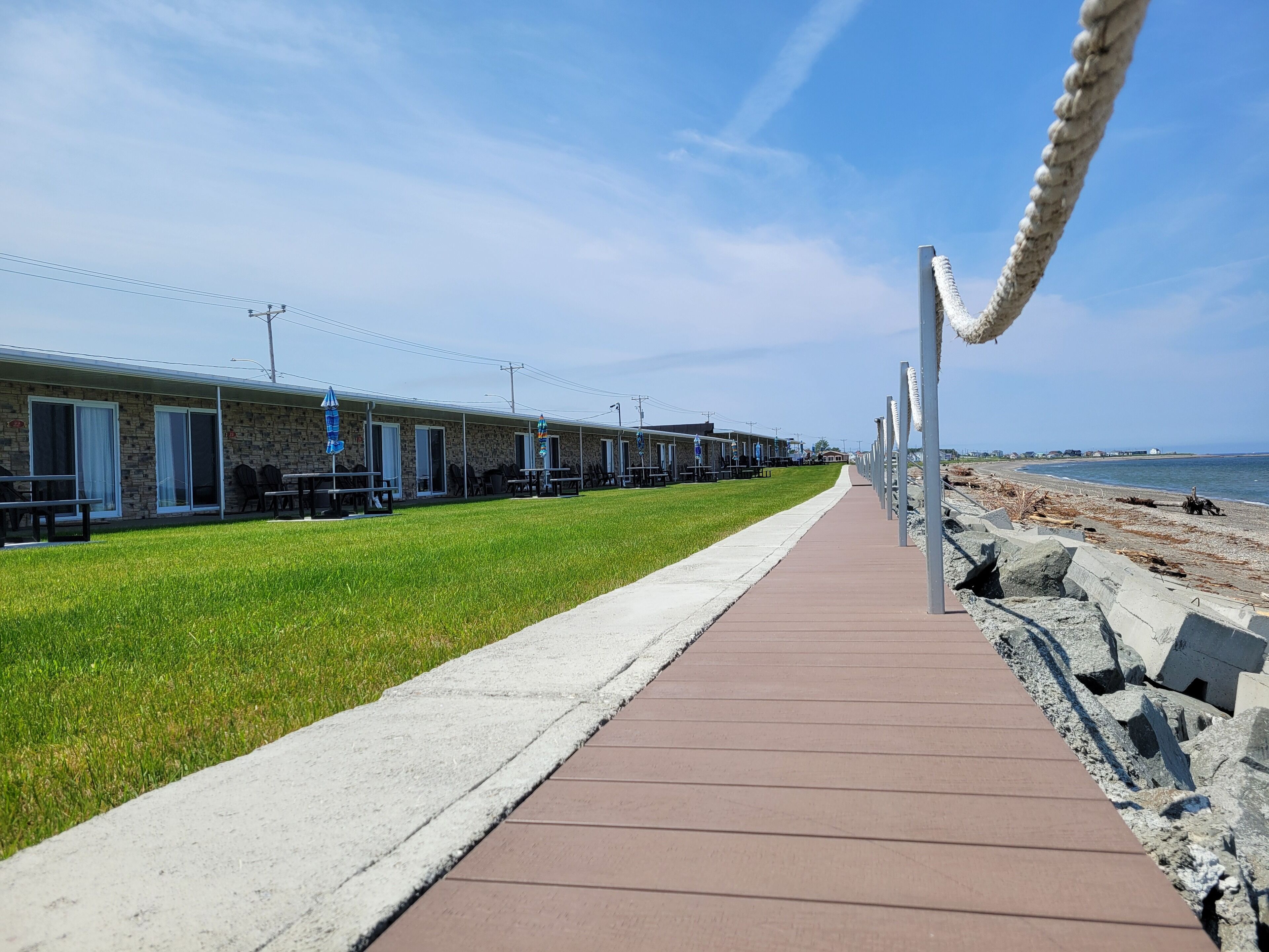 Une promenade en bord de mer bordée de cabanes, avec un espace herbeux et une vue sur l’océan.