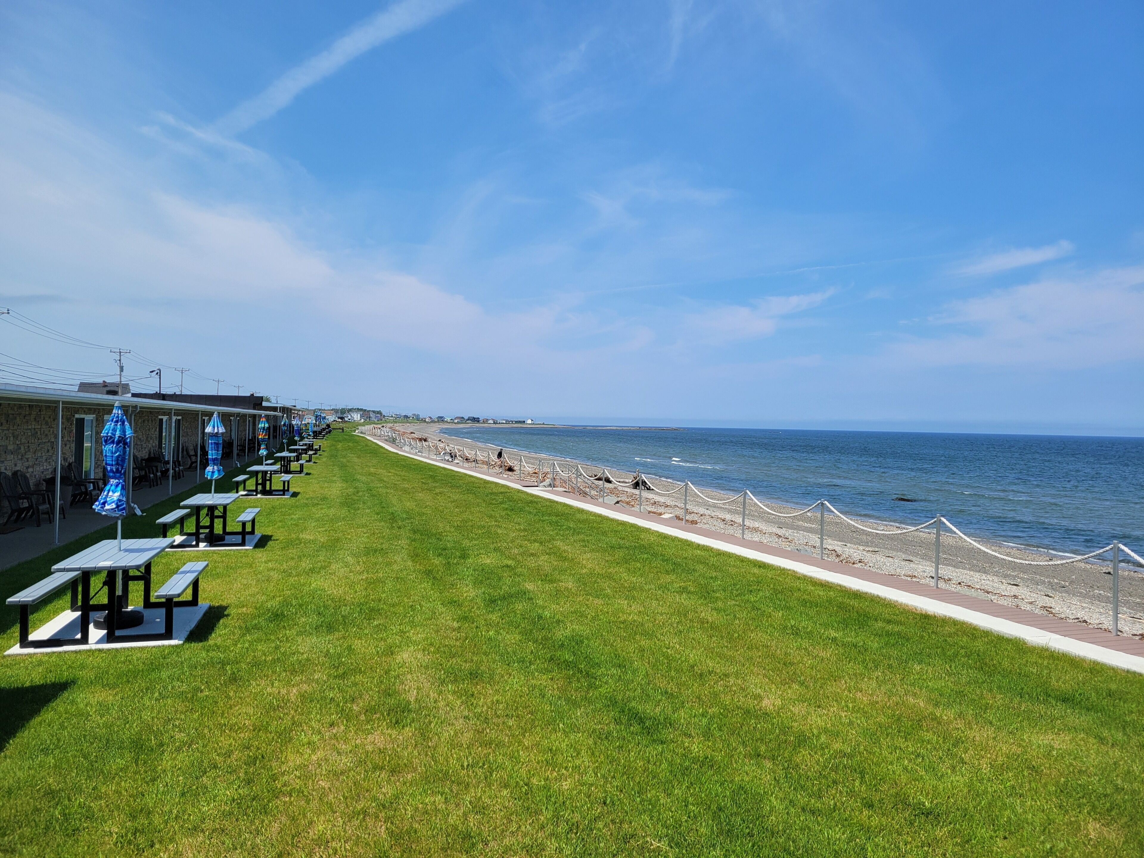 A seaside patio with picnic tables and umbrellas, a grassy area, and a view of the ocean.