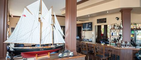 Een barruimte met een model zeilboot, houten stoelen en een televisie aan de muur.