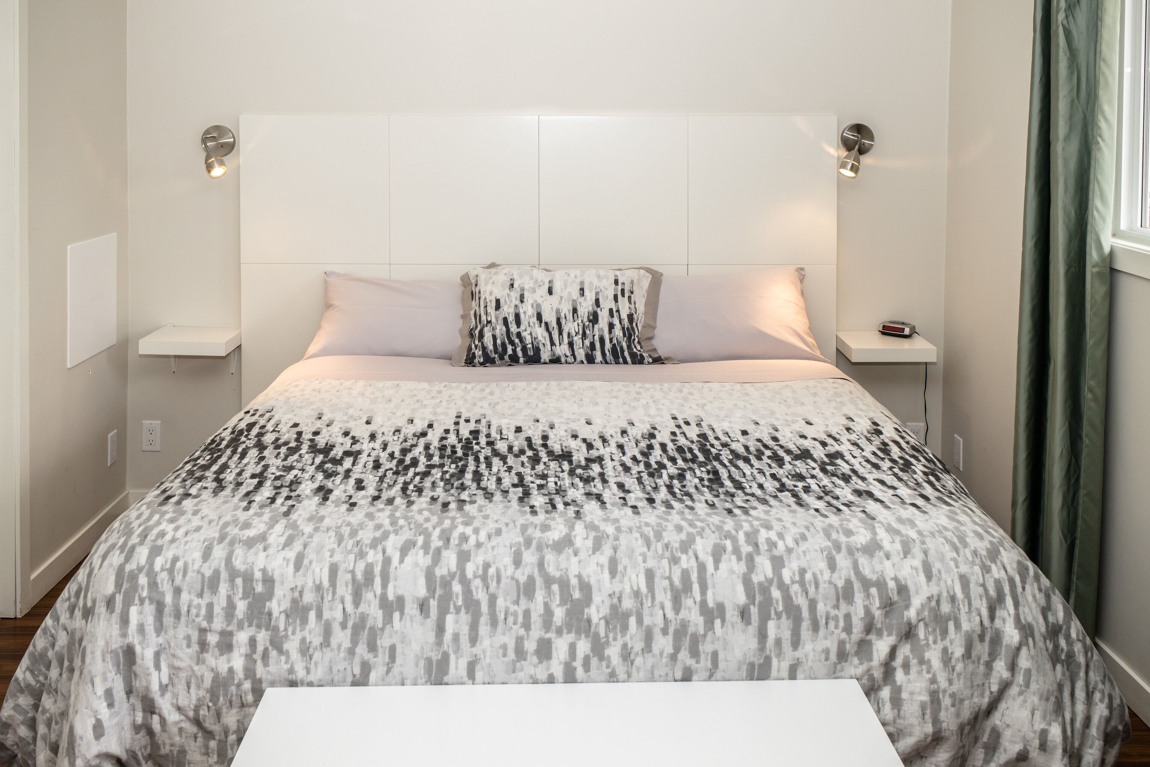 Quarto moderno com colcha estampada, mesas de cabeceira e iluminação embutida na parede.