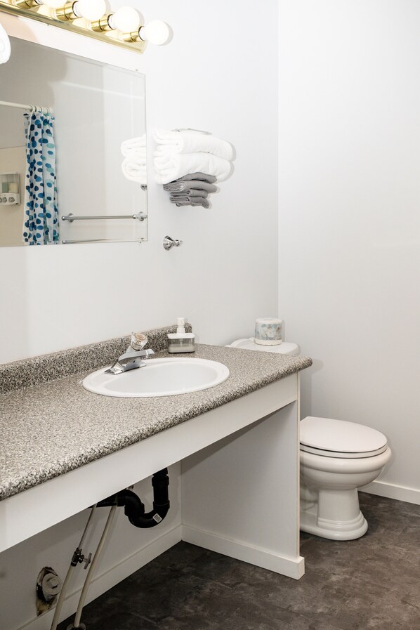 Un baño con lavamanos, espejo y retrete blancos. Hay toallas y artículos de aseo en la encimera.