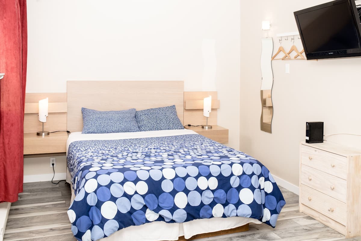 A bedroom with a bed, bedside tables, a TV, and a dresser.