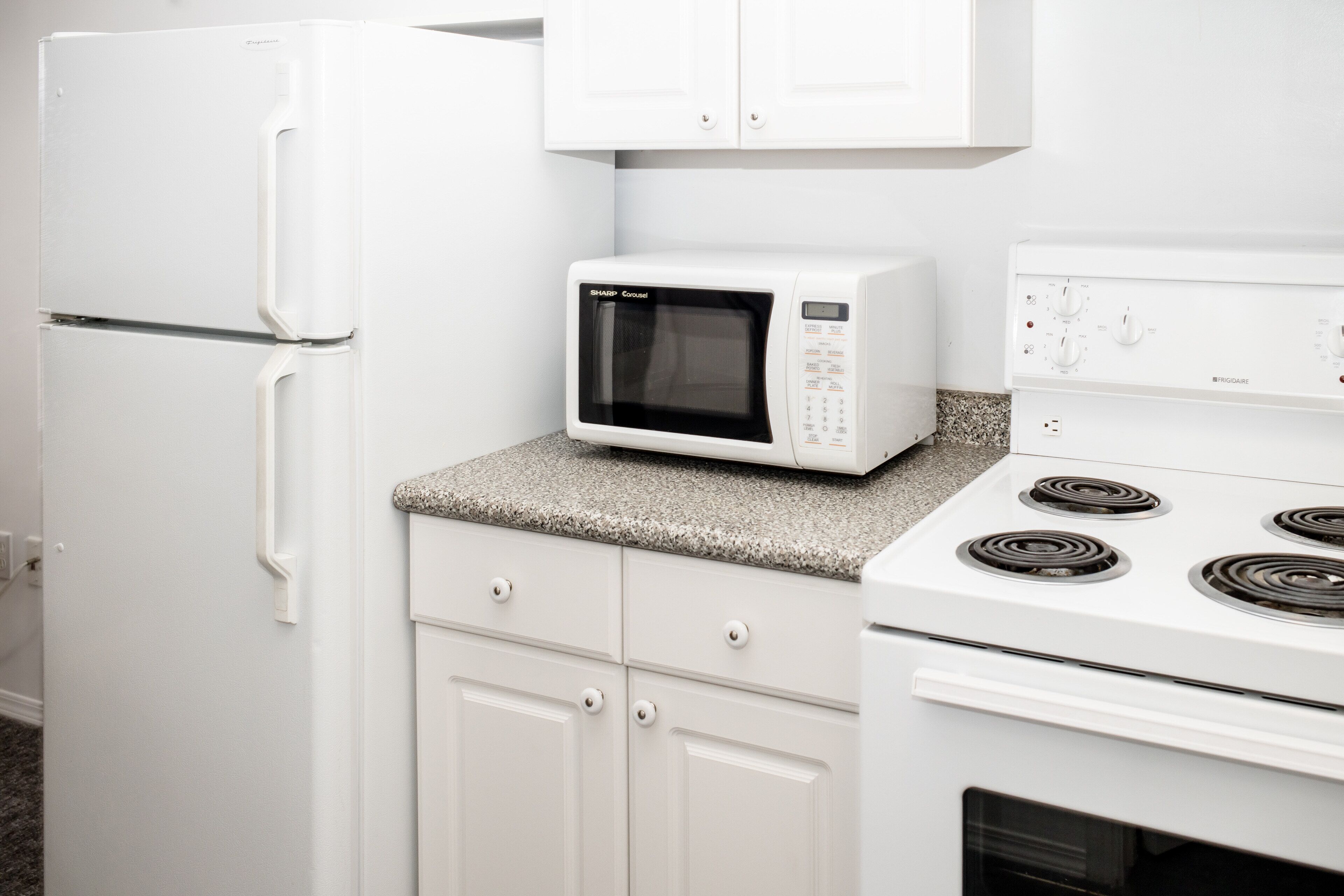 A kitchen with a white refrigerator, microwave, stove, and granite countertop.