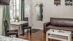 Una habitación con una cama, un sofá de cuero marrón, una mesa de centro blanca, una mesa de comedor con sillas y un espejo en la pared.