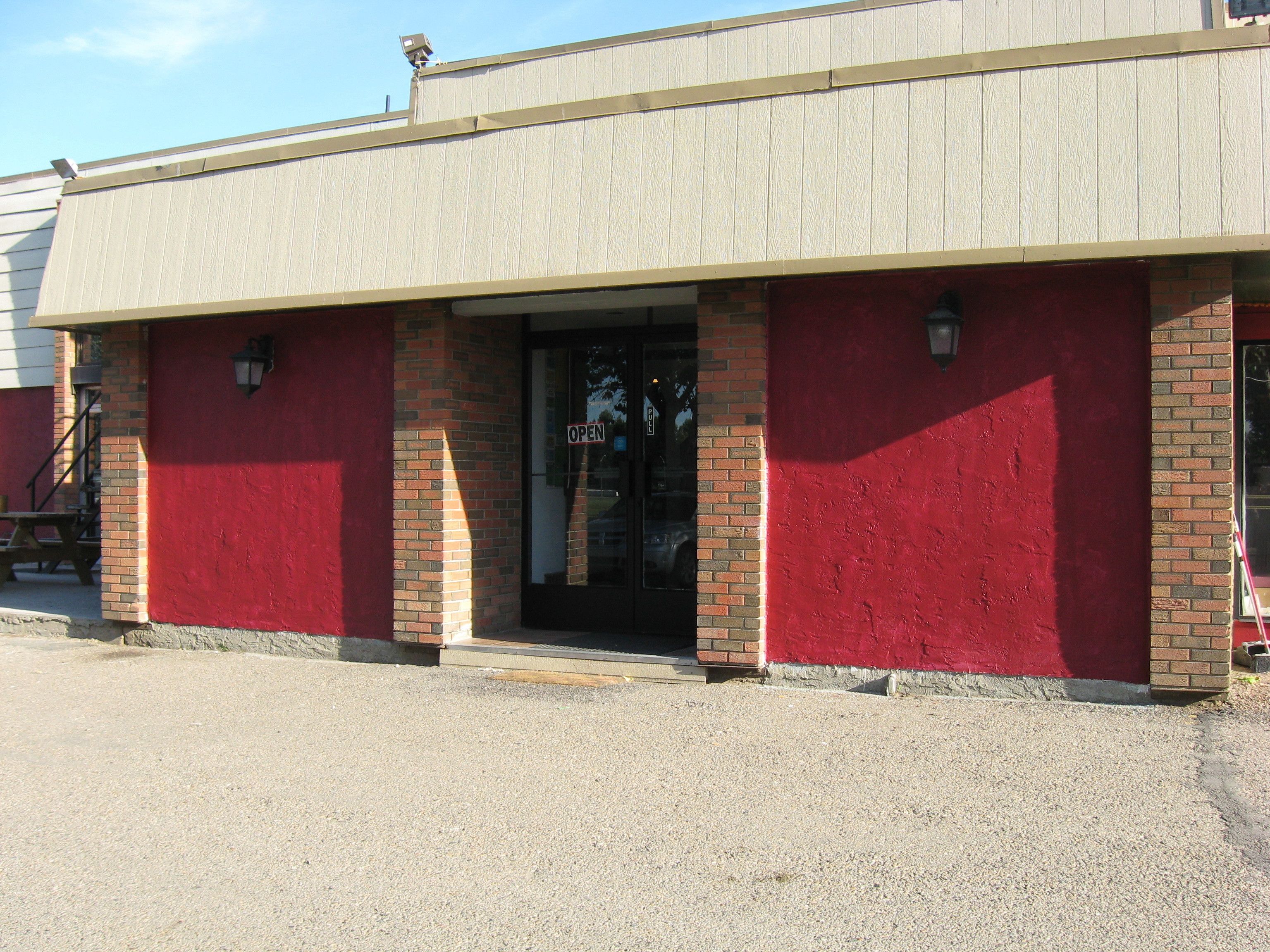 A building with a red facade, a brick entrance, and a sign indicating it is open.