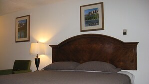 A neatly made bed with a wooden headboard, a green chair, and two framed pictures on the wall. - Royal City Motor Inn (Brooks)