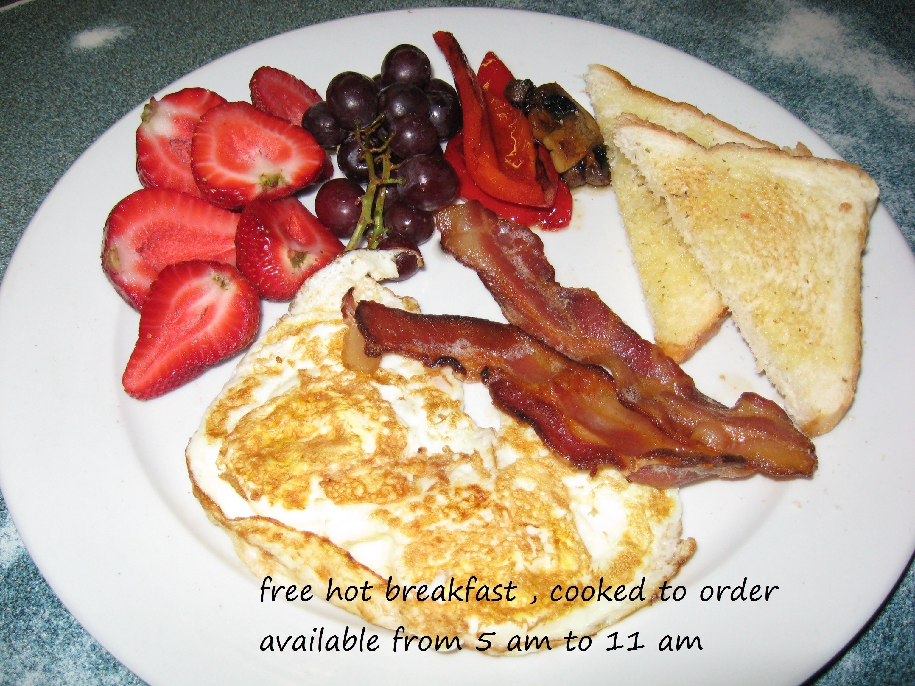 A plate of breakfast with eggs, bacon, toast, strawberries, and grapes.