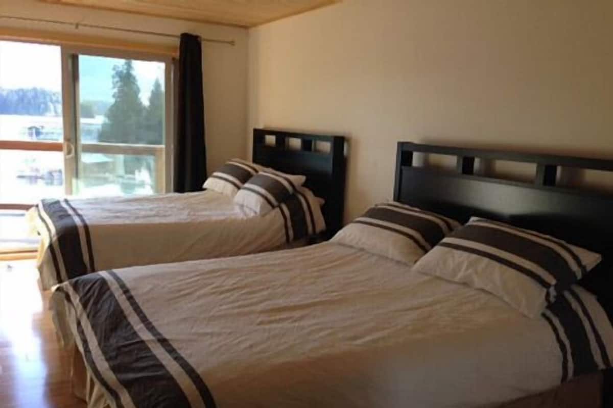 Quarto com duas camas, cada uma com roupa de cama listrada e cabeceiras escuras, localizado perto de uma janela com vista para árvores.