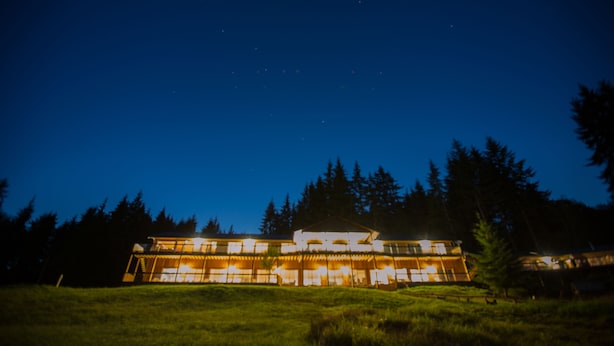 A large, modern building with multiple levels and large windows, surrounded by a grassy area and trees. - Kagoagh Resort and Fishing Lodge (Quatsino)