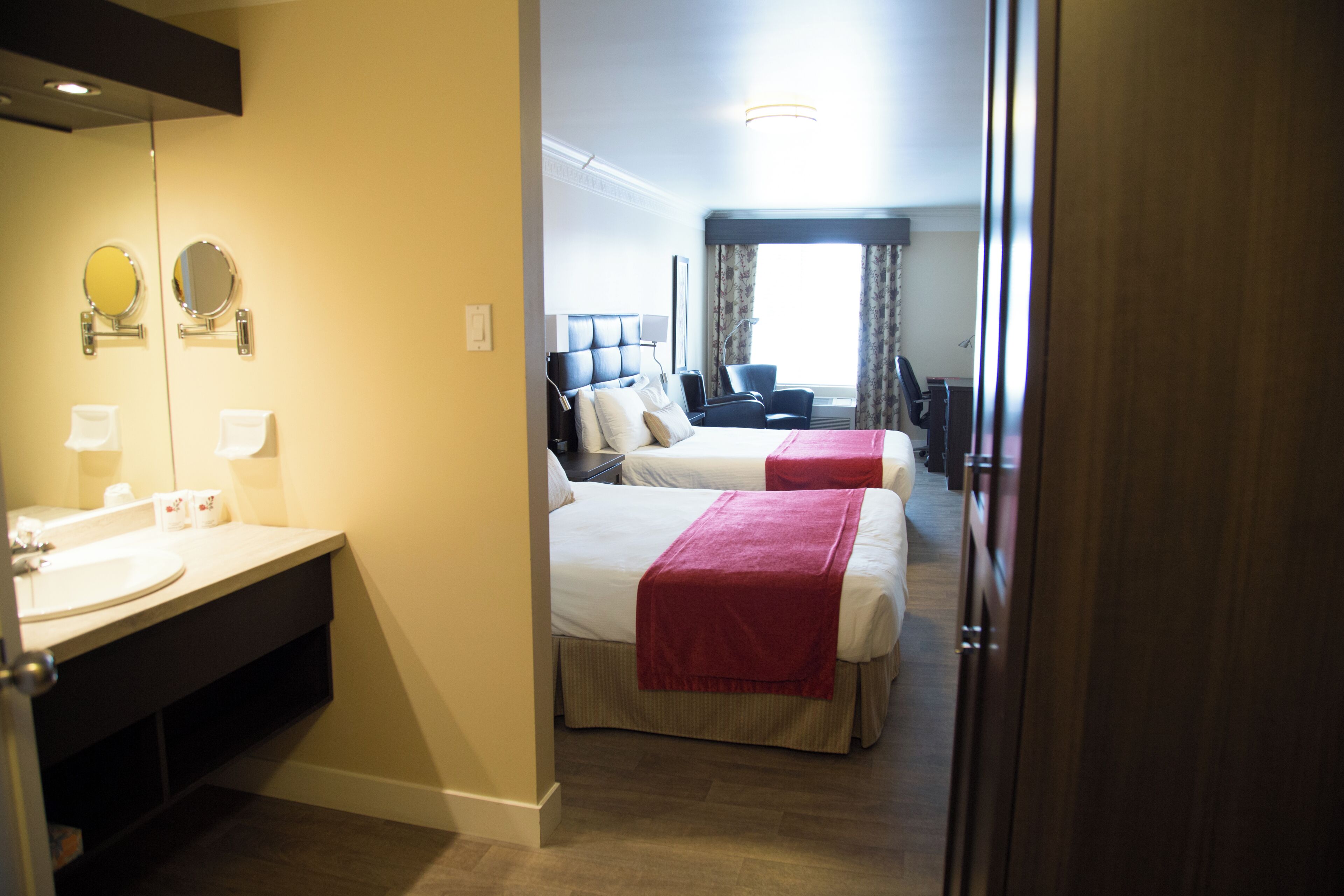 Une chambre d’hôtel avec salle de bain, deux lits, un bureau et une chaise.