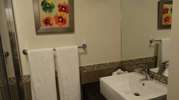 Une salle de bain avec un lavabo blanc, un miroir et un porte-serviettes sur lequel sont posées deux serviettes blanches. Un tableau encadré représentant des fleurs est accroché au mur.