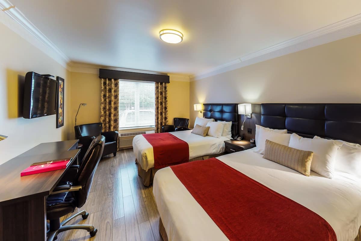 A hotel room with two beds, a desk, a chair, a TV, and a window with curtains.