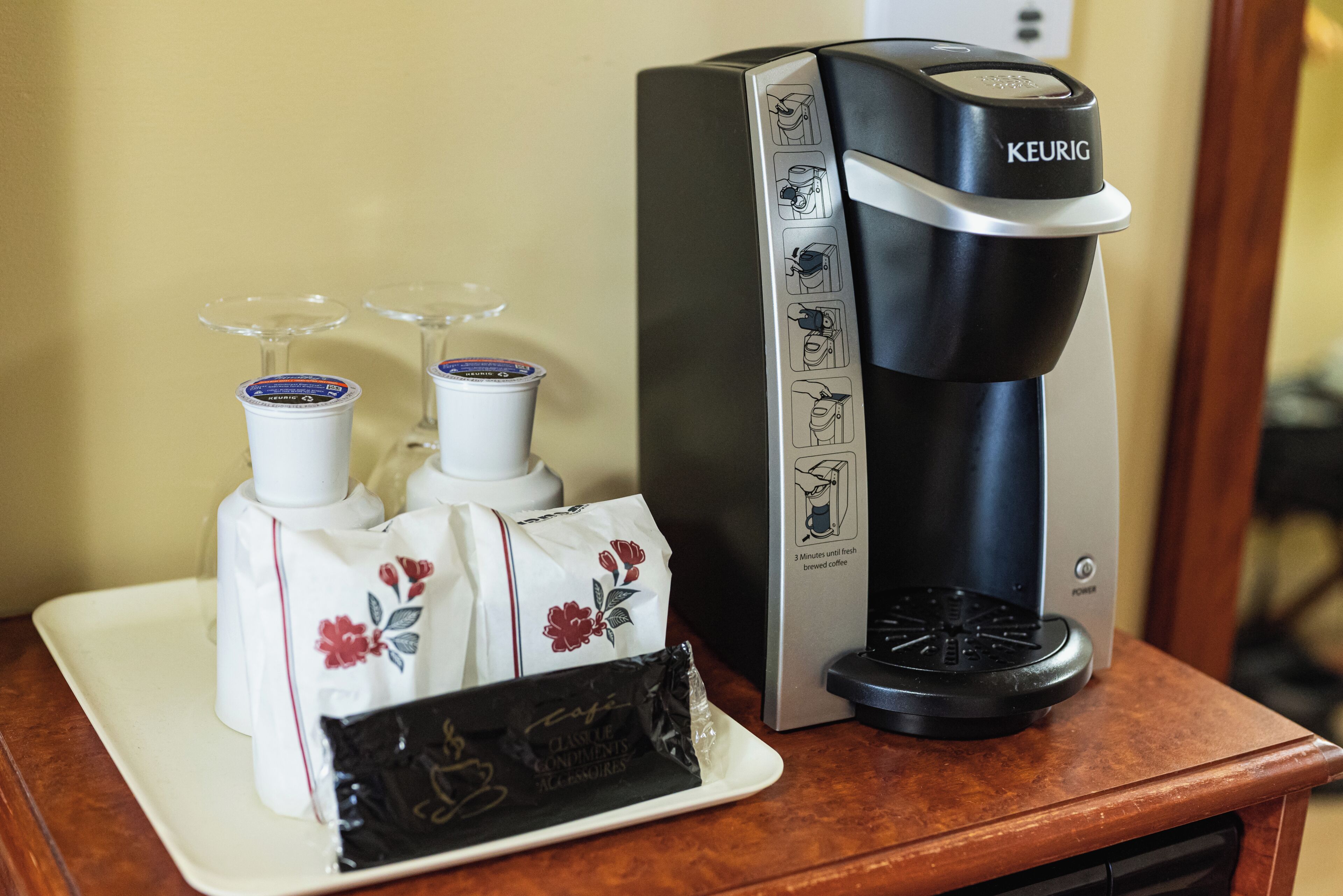 A Keurig coffee maker with a coffee pod and two glasses on a tray.