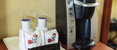 A Keurig coffee maker with a coffee pod and two glasses on a tray.