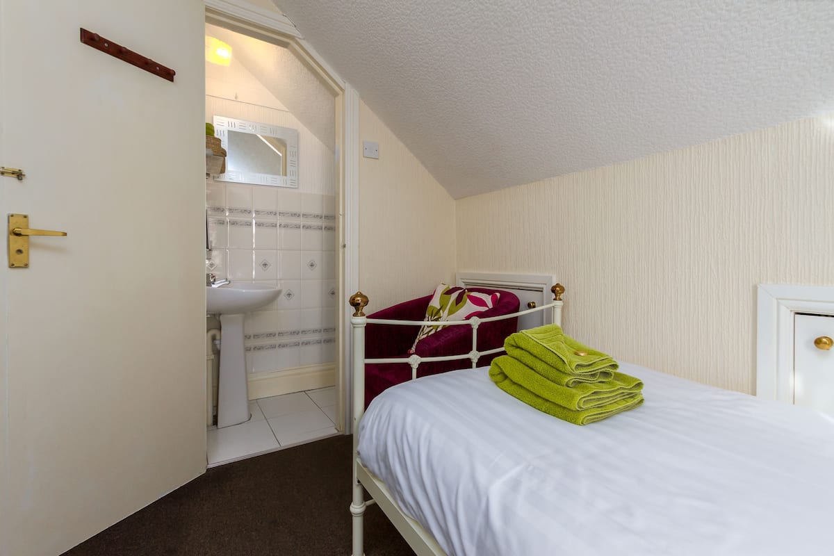 Un dormitorio con cama, mesita de noche, ventana y puerta que da a un baño.