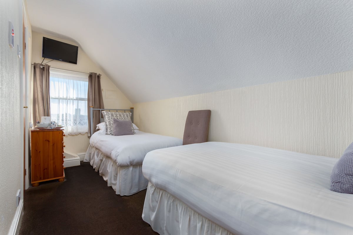 Un dormitorio con dos camas individuales, un aparador de madera, un televisor montado en la pared y una ventana con cortinas.