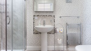 Une salle de bain avec une douche à parois de verre, un lavabo sur colonne, un porte-serviettes et des toilettes.