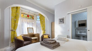 Une chambre d’hôtel comprenant un lit, un bureau, une chaise, un miroir et une salle de bain avec un lavabo et un miroir.