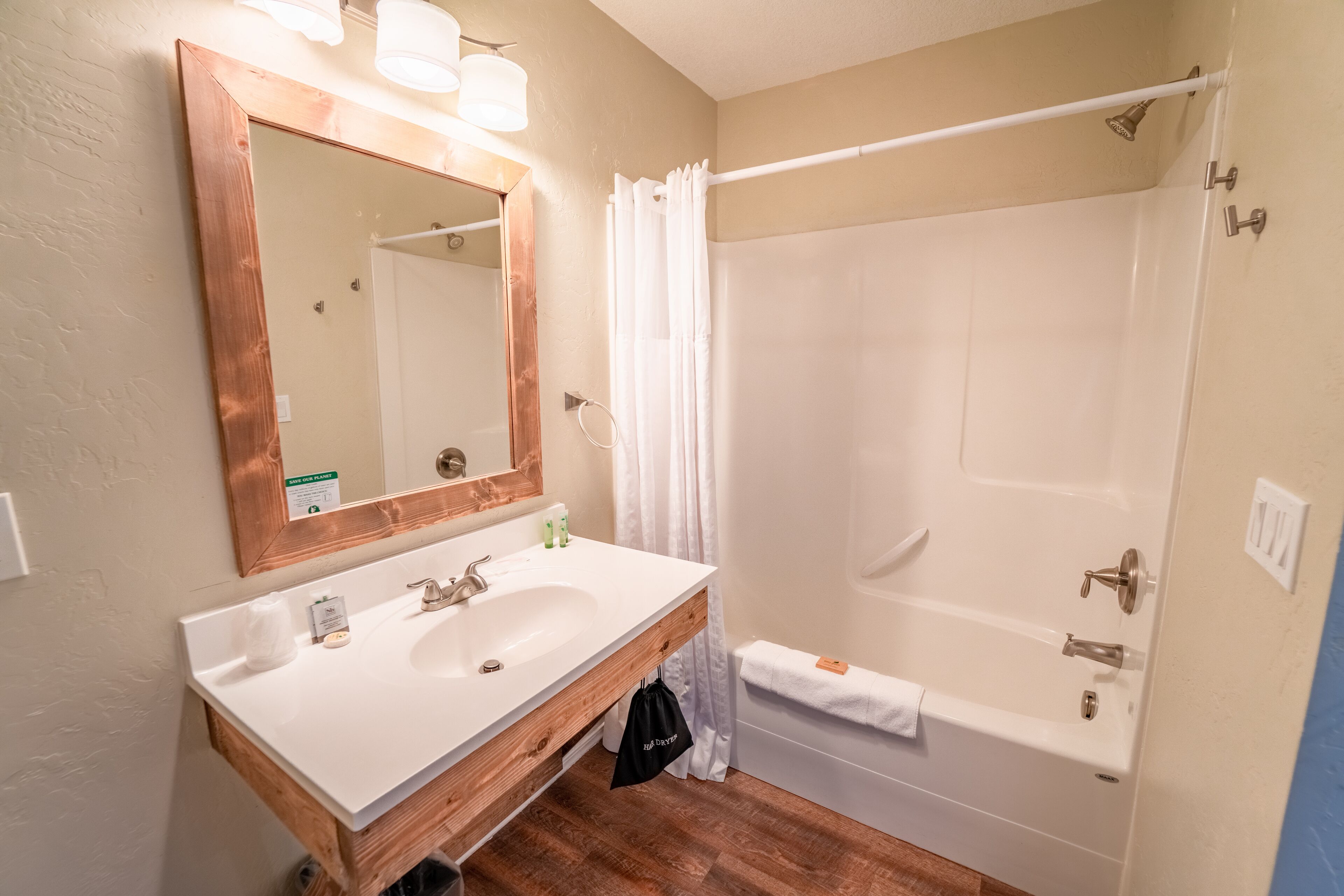 Une salle de bain avec un meuble-lavabo en bois, deux vasques, un grand miroir, une douche avec un rideau et un porte-serviettes.