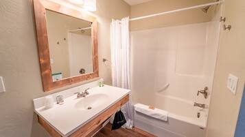 Une salle de bain avec un meuble-lavabo en bois, deux vasques, un grand miroir, une douche avec un rideau et un porte-serviettes.