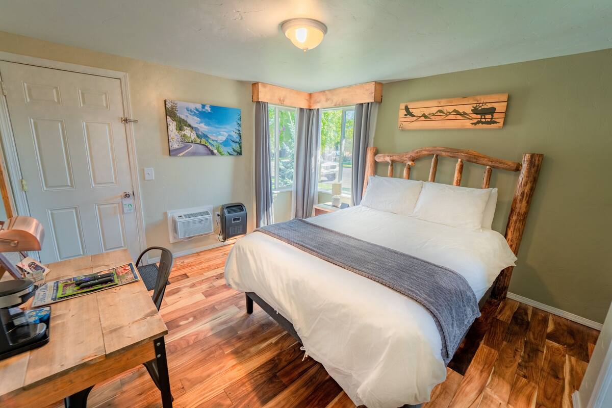 A bedroom with a wooden bed, a desk with a lamp, and a painting on the wall.