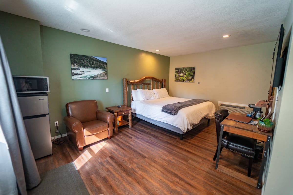 A bedroom with a bed, a desk, a chair, a television, and a refrigerator.