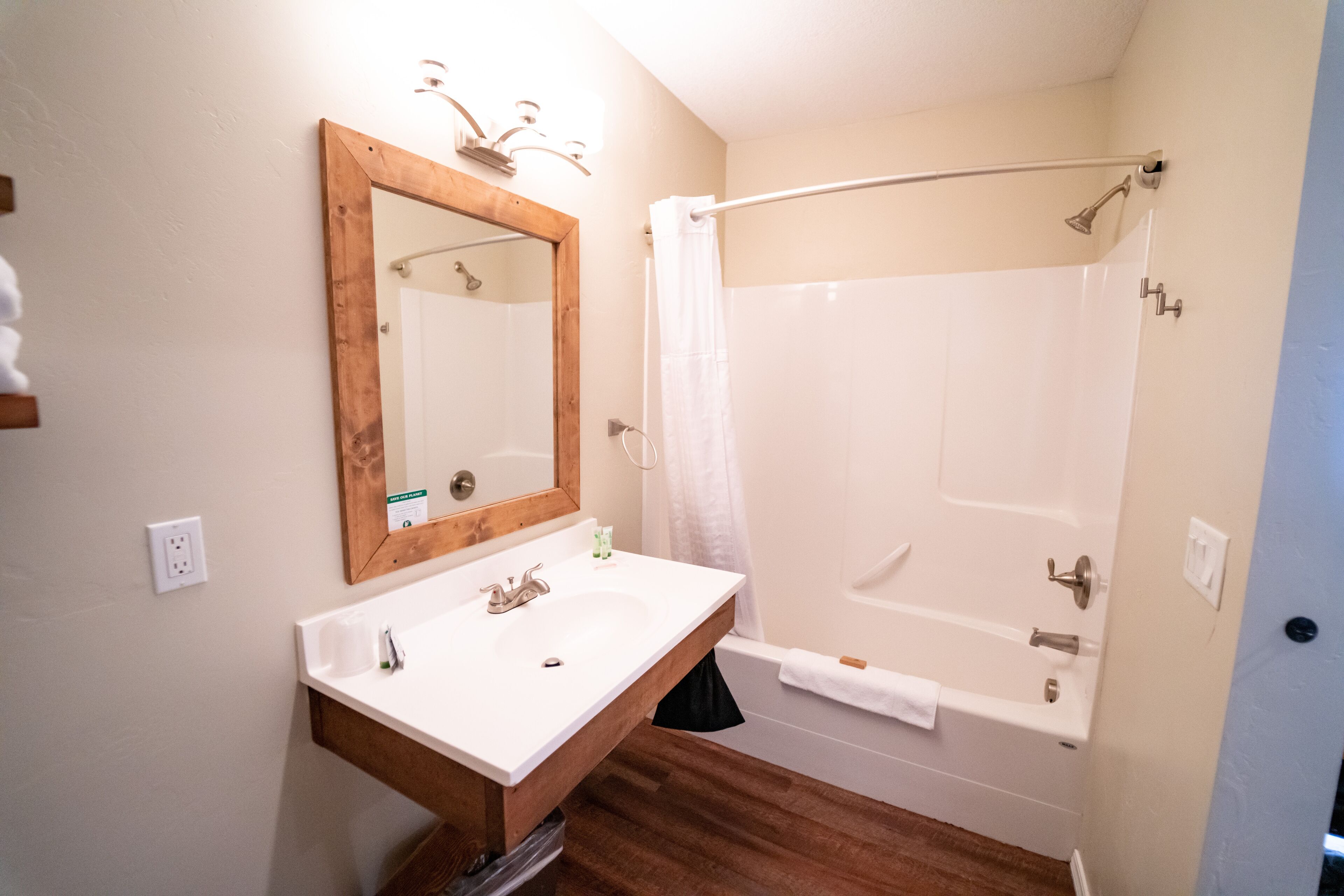 A bathroom with a wooden vanity, a large mirror, a bathtub, and a shower curtain.