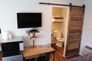 Habitación compacta con televisor de pantalla plana, microondas, una pequeña mesa con una revista y una puerta corredera que da al baño.