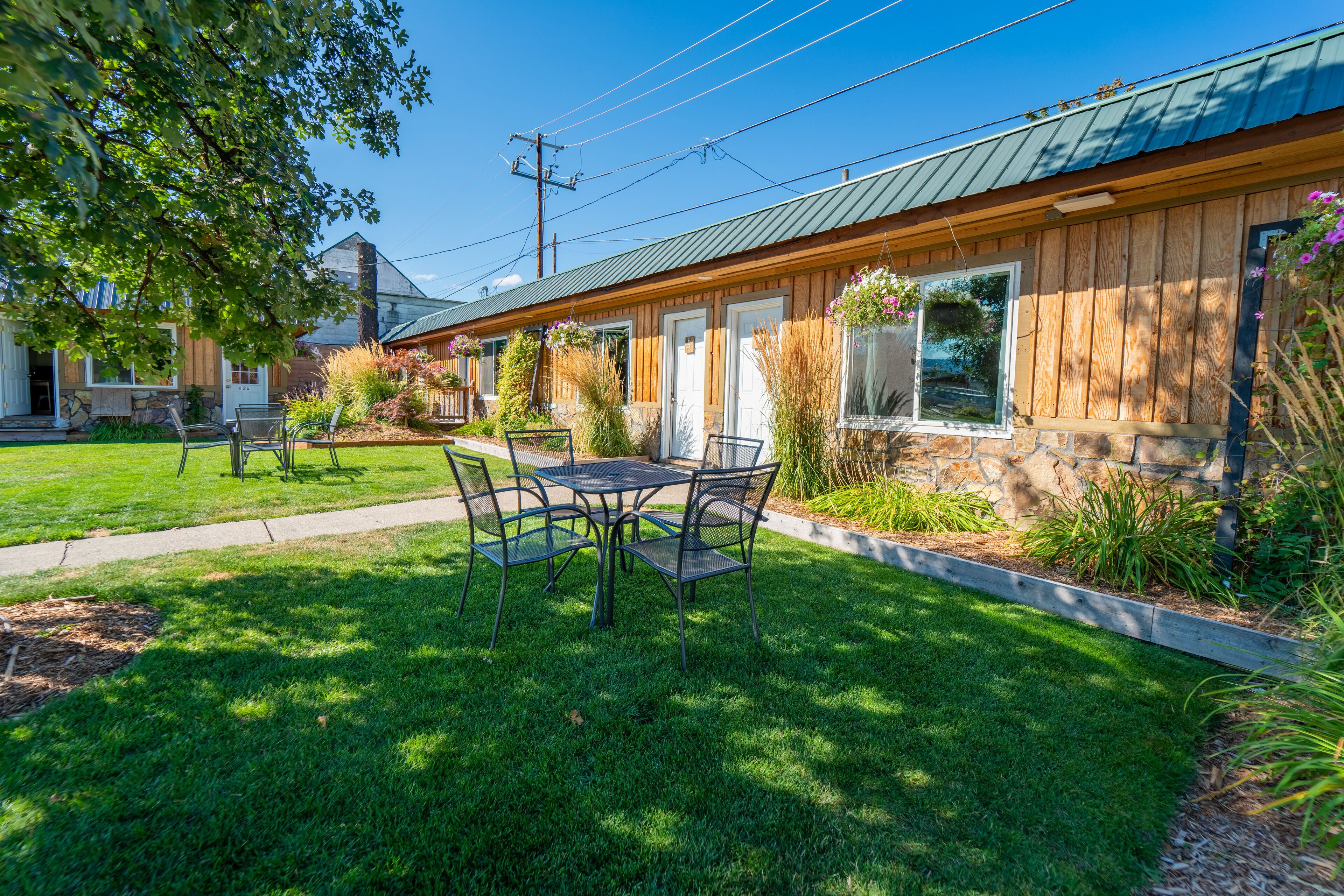A wooden building with a green roof, a patio with a table and chairs, and a well-maintained lawn.