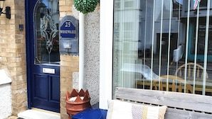 A blue door with a number plate, a bench with cushions, and a window with a flag. - Westward Bed & Breakfast (Newquay)