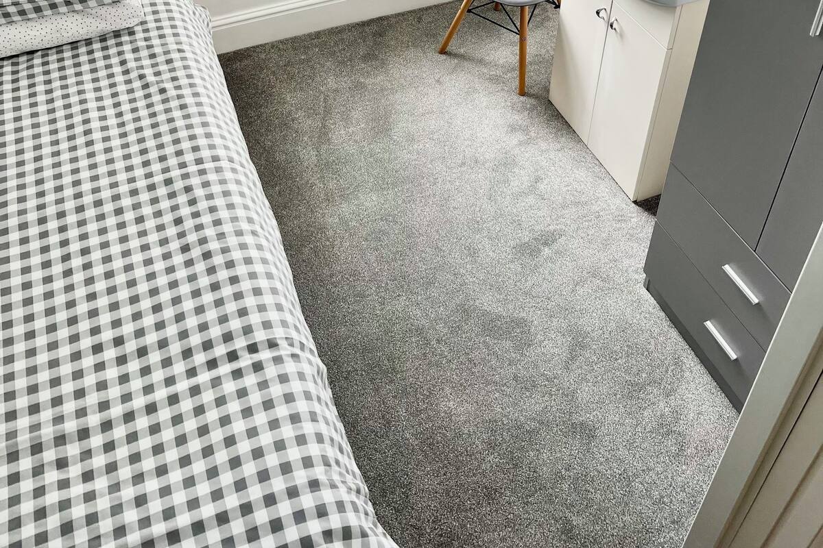 A bedroom with a checkered bedspread, a grey chair, a white sink, and a cabinet.